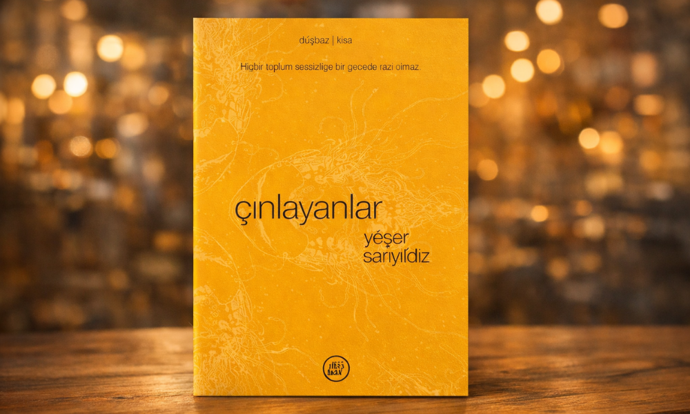 Görselde sarı tonlarda tasarlanmış bir kitap kapağı, ahşap bir yüzey üzerinde dik şekilde duruyor. Arka planda sıcak ışıklarla oluşmuş, bulanık ve altın rengi bir bokeh efekti yer alıyor. Kapakta “çınlayanlar” başlığı ve altında yazar adı olarak “yeşer sarıyıldız” yazıyor. Üst bölümde “düşbaz | kısa” ve “Hiçbir toplum sessizliğe bir gecede razı olmaz.” cümlesi bulunuyor. Sade ama parlak tasarım, kitaba hem şiirsel hem de dikkat çekici bir atmosfer kazandırıyor.