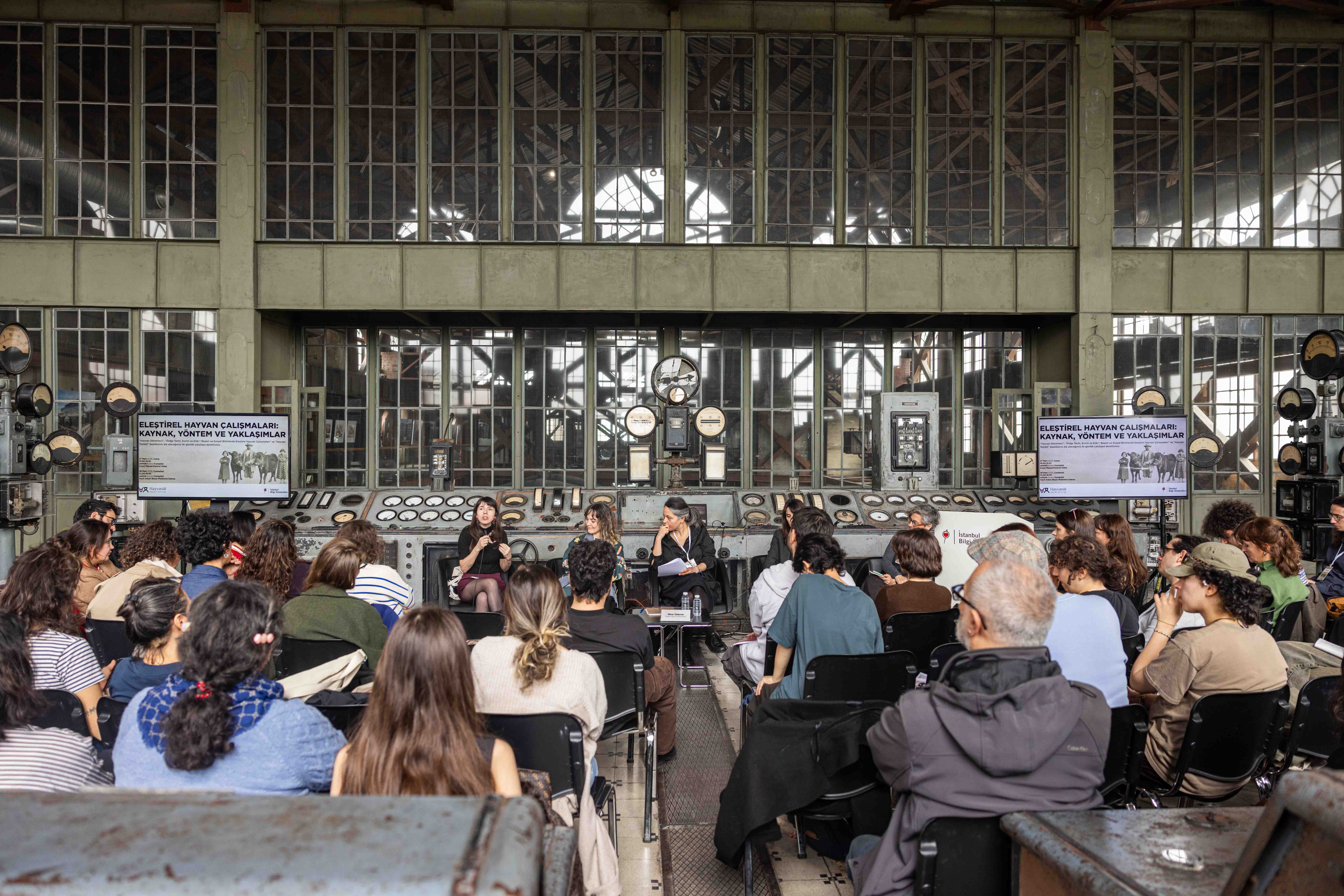 bilgi üniversitesinde herkesin arkadan göründüğü çalıştaı dinleyen insanlar görünmekte.