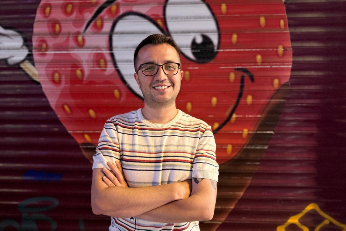 Yıldız Tar graffitili bir duvar önünde poz vermiş, gülümsüyor ve kollarını kavuşturmuş.